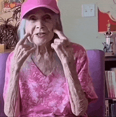 an elderly woman wearing a pink hat and a pink shirt is making a peace sign