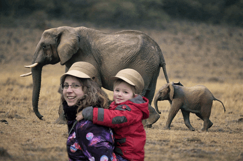 a woman holds a child in front of an elephant