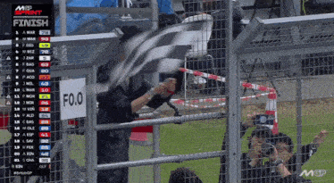 a man waving a checkered flag behind a fence with a finish sign above him