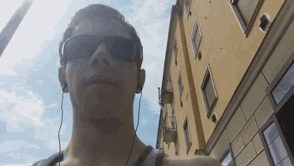 a man wearing sunglasses and ear buds is standing in front of a building