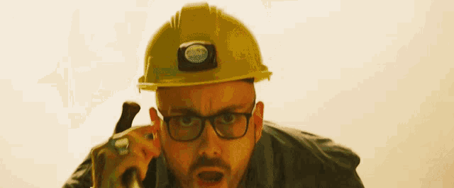 a man wearing a hard hat and glasses is holding a hammer in his hand