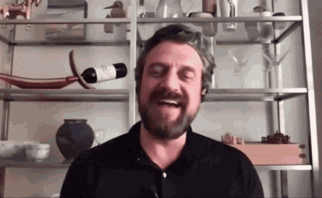 a man with a beard is laughing in front of a wine rack
