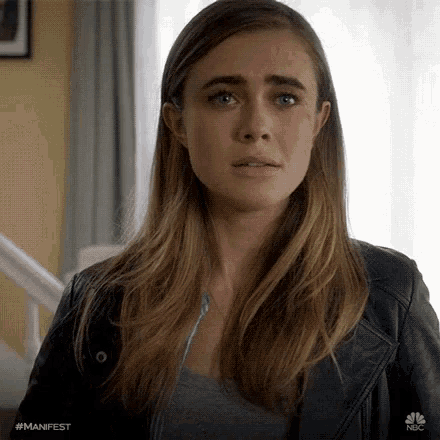 a woman wearing a leather jacket and a gray shirt is looking at the camera .
