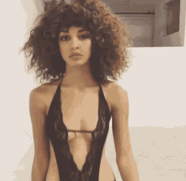 a woman with curly hair is wearing a black lace bodysuit with a plunging neckline