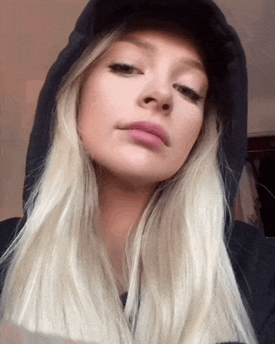 a blonde woman wearing a black hat and a black hoodie looks at the camera