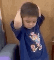 a young boy is covering his ears with his hands while wearing a blue shirt .