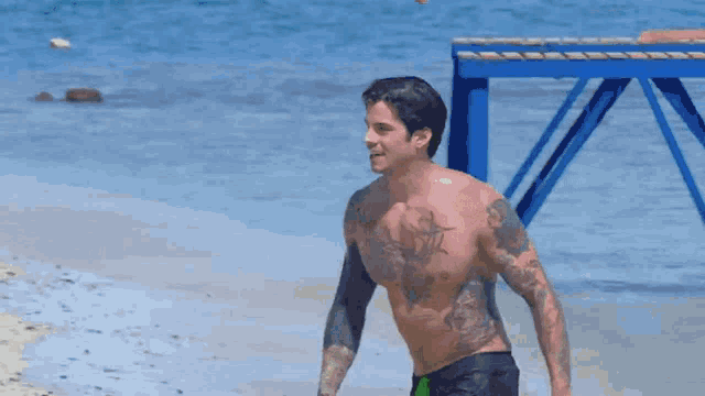 a shirtless man with tattoos on his arms and chest is standing on a beach