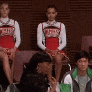 a group of cheerleaders wearing wmhs uniforms are sitting in a row .