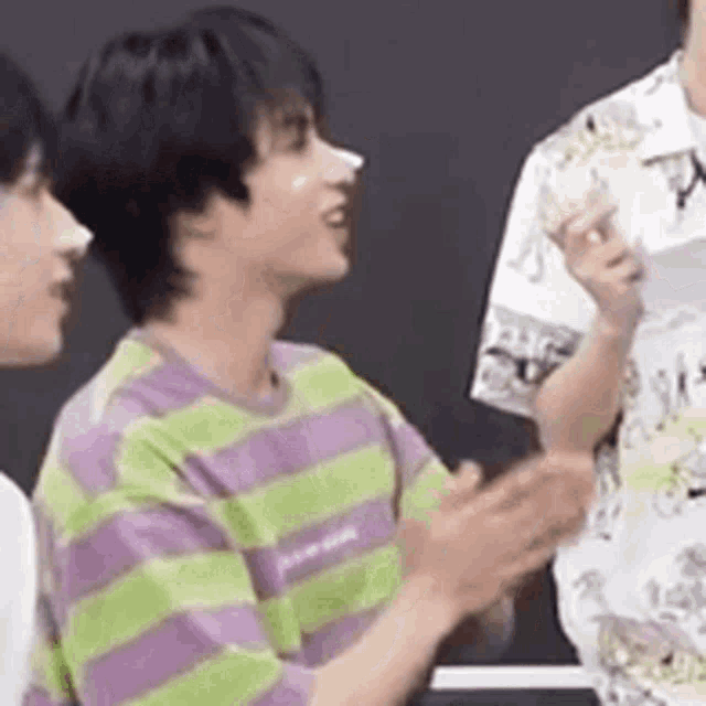 a man in a green and purple striped shirt is clapping his hands while standing next to another man .