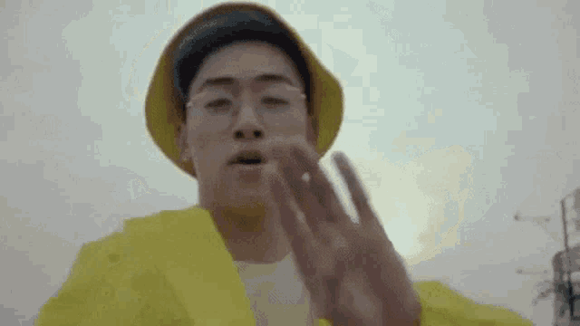 a young man wearing a yellow jacket and a yellow hat is making a stop sign with his hands .