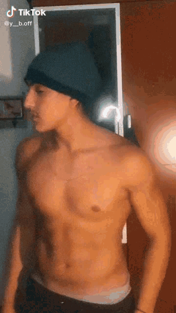a shirtless man wearing a beanie is standing in front of a mirror and looking at himself .