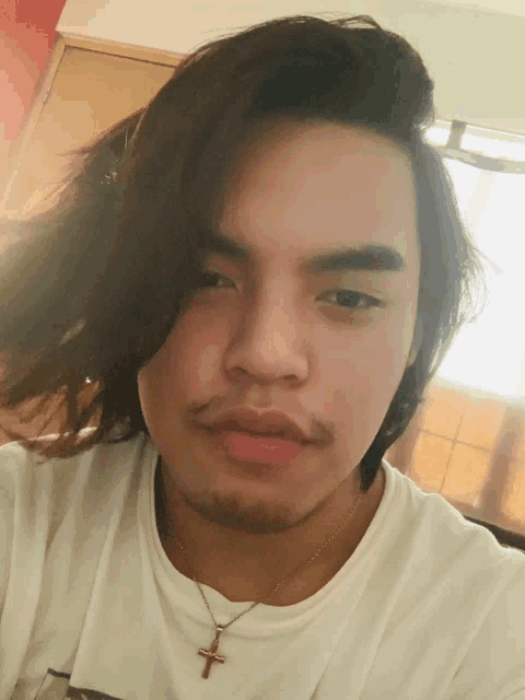 a young man wearing a white shirt and a cross necklace