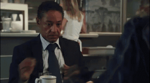 a man in a suit and tie sits at a table with a cup of coffee in front of him