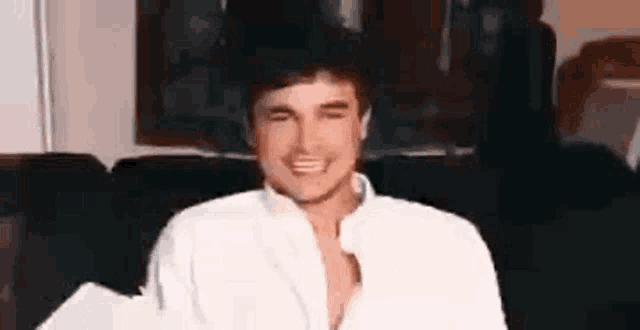 a man wearing a white shirt is sitting on a couch and smiling .