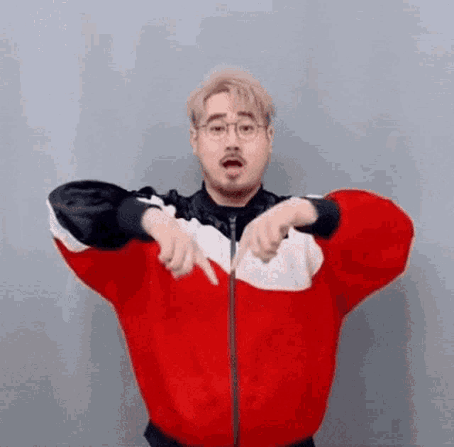 a man wearing a red and white jacket and glasses is pointing at the camera .