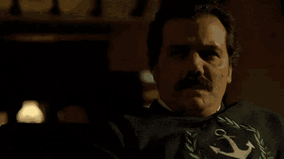 a man with a mustache is wearing a black sweater with an anchor on it