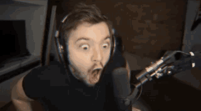 a man wearing headphones stands in front of a microphone with a surprised look on his face