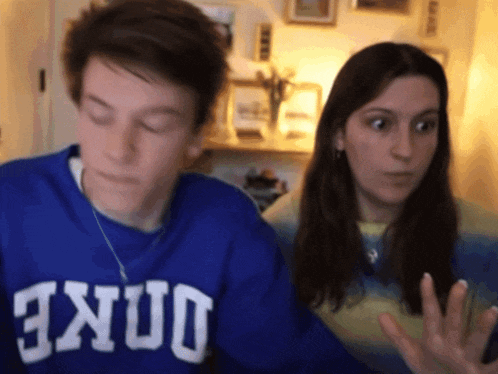 a man wearing a blue duke sweatshirt stands next to a woman with her eyes closed