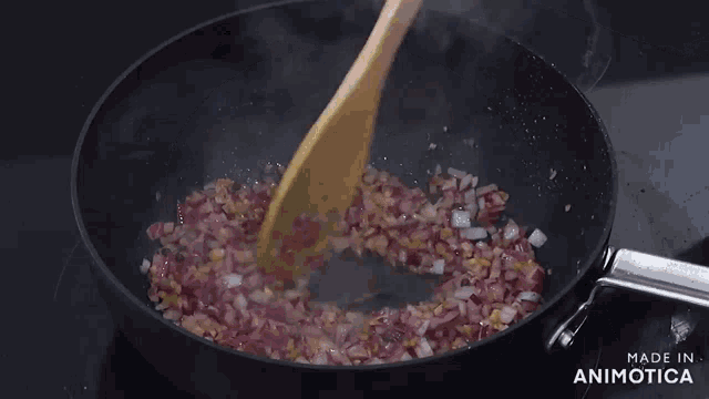 a wooden spoon is stirring onions in a frying pan .