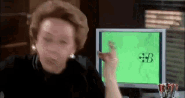 a woman is sitting at a desk in front of a computer screen with a green screen .