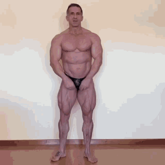 a muscular man in a black bikini is standing in front of a white wall
