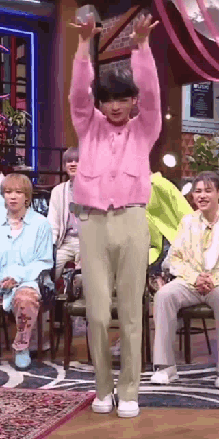 a man in a pink sweater and khaki pants is dancing in front of a group of people .