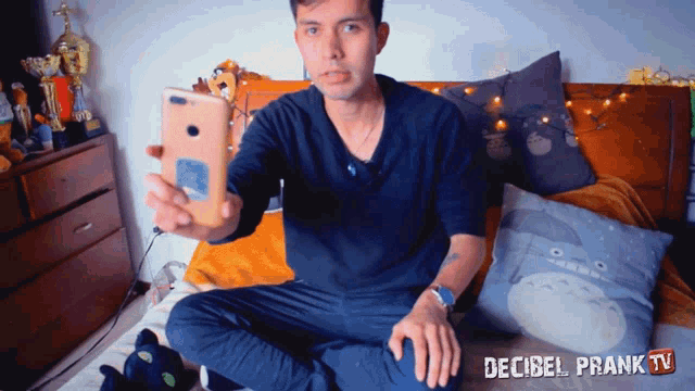 a man sits on a bed holding a cell phone with decibel prank tv written on the bottom