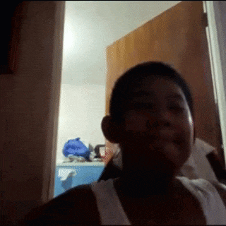 a young boy in a white tank top is smiling in a dark room