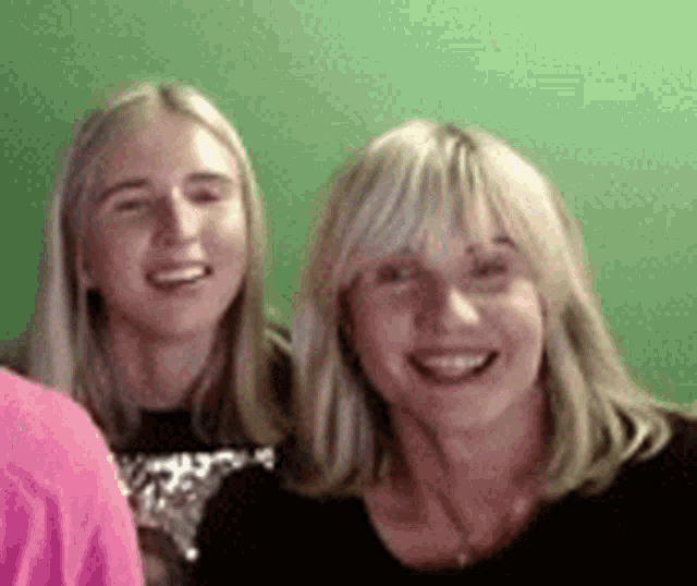 two women are posing for a picture together and smiling in front of a green screen .