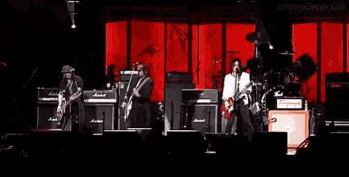 a group of men are playing guitars on a stage in front of a red wall .