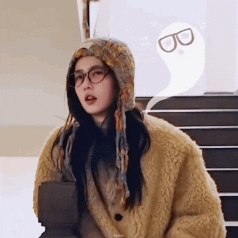a woman wearing glasses and a hat is standing in front of a staircase .