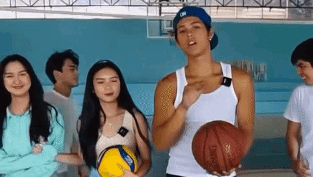 a man in a white tank top is holding a basketball while standing next to a woman holding a volleyball .