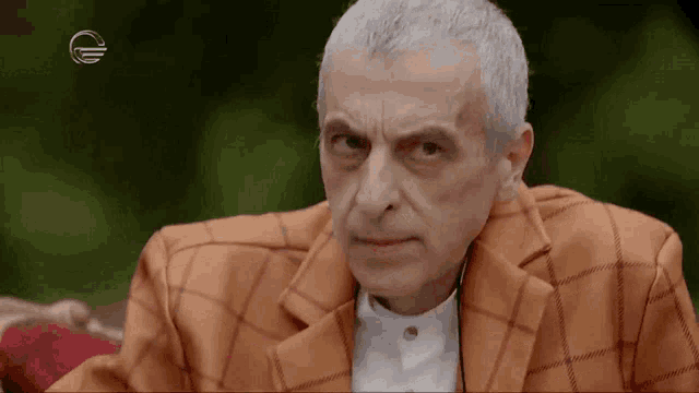 a man with gray hair and a plaid jacket is making a funny face .