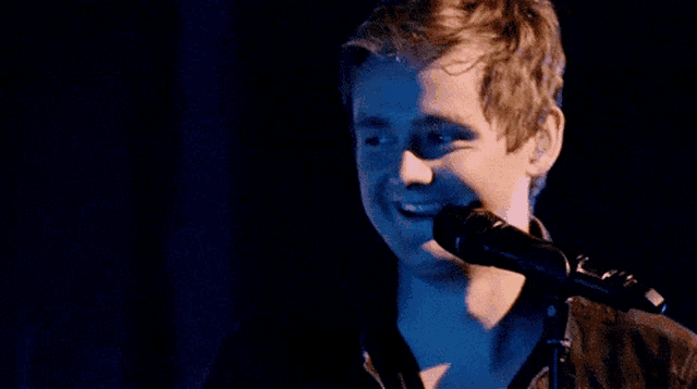 a young man singing into a microphone with a blue background