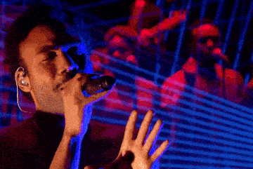 a man singing into a microphone with a reflection of a man in the background
