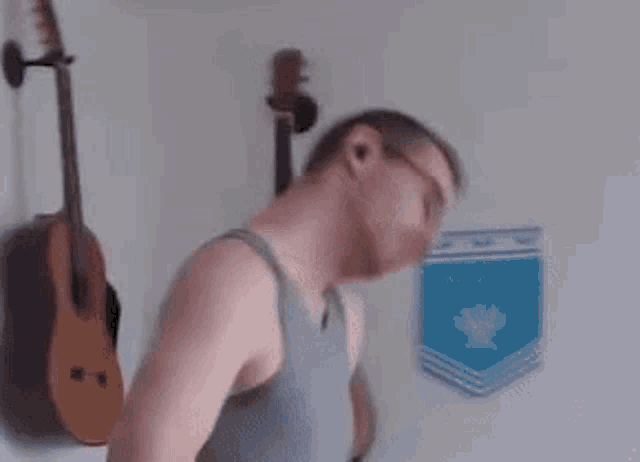 a man in a tank top is standing in front of a wall with guitars on it .
