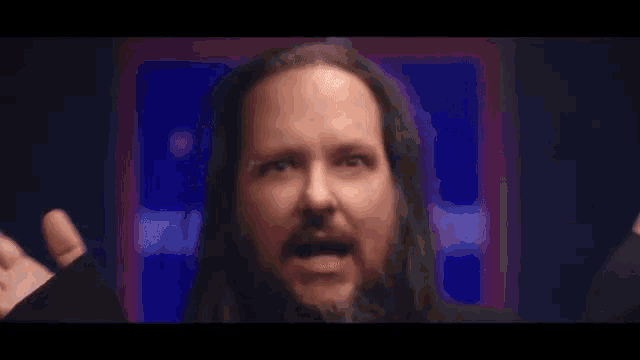 a man with long hair and a beard is making a face with his hands outstretched .