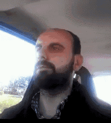 a man with a beard is sitting in a car looking out the window