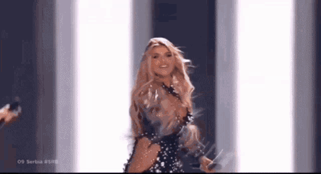 a woman in a black dress is dancing on a stage with a microphone in her hand .