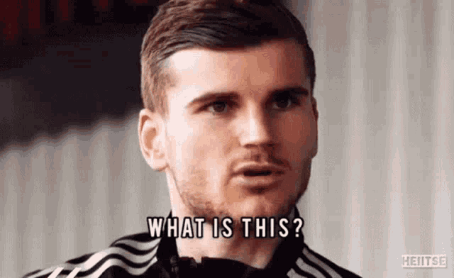 a man with a beard is asking what is this while wearing a black and white adidas jacket .
