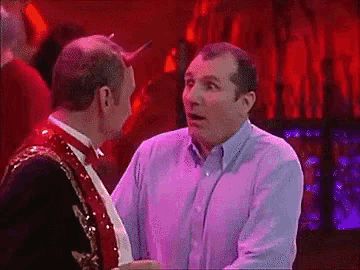 a man in a purple shirt is talking to another man in a red suit