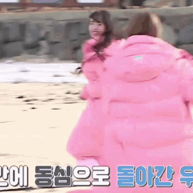 a couple of women in pink jackets are standing on a beach .