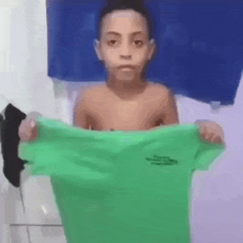 a shirtless young boy is holding a green shirt in his hands .