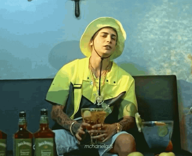 a man in a yellow shirt is sitting on a couch with bottles of jack daniels behind him