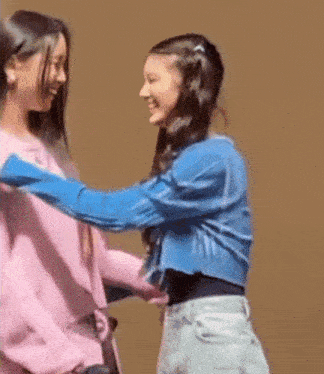 two young girls are hugging each other and laughing while standing next to each other .