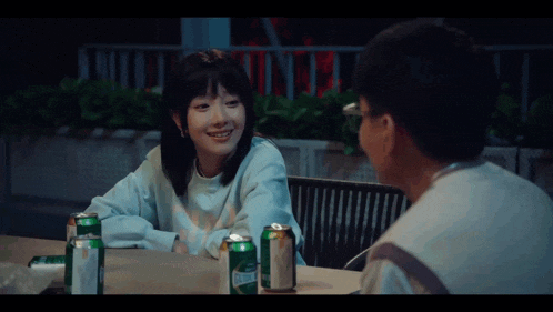 a man and a woman are sitting at a table with cans of beer .