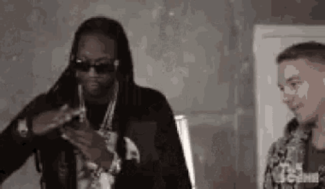 two men are standing next to each other in a room and one of them is wearing sunglasses .