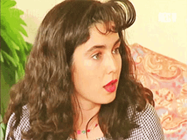 a woman with long curly hair is sitting on a couch and looking at the camera .