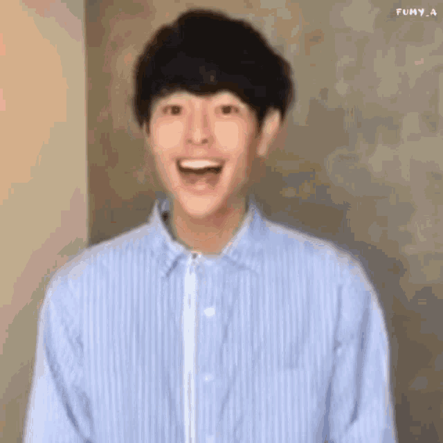 a young man wearing a blue striped shirt is laughing and smiling .