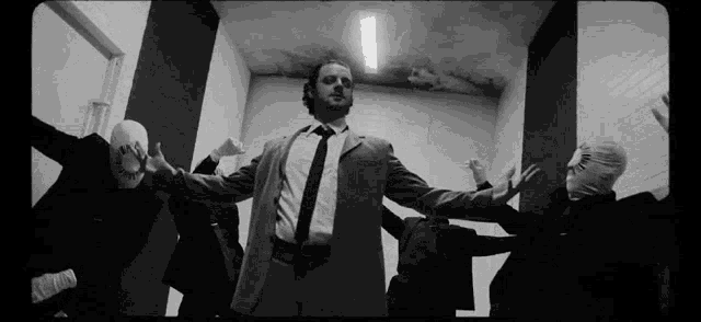 a black and white photo of a man in a suit and tie surrounded by masked men